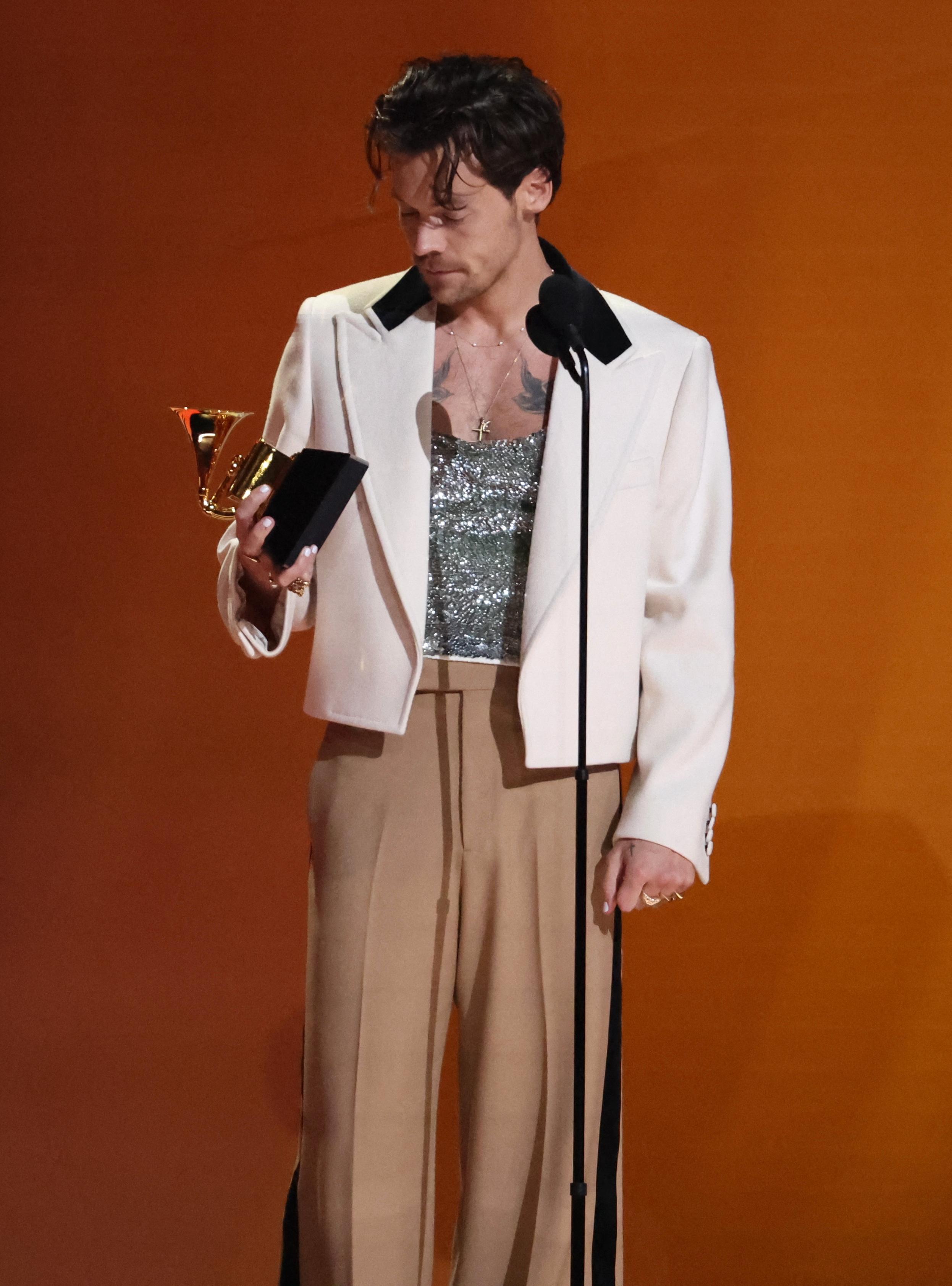 Harry Styles mottar prisen «Album of the Year» iført en glitrende topp, brun bukse og en jakke i svart og hvitt.
