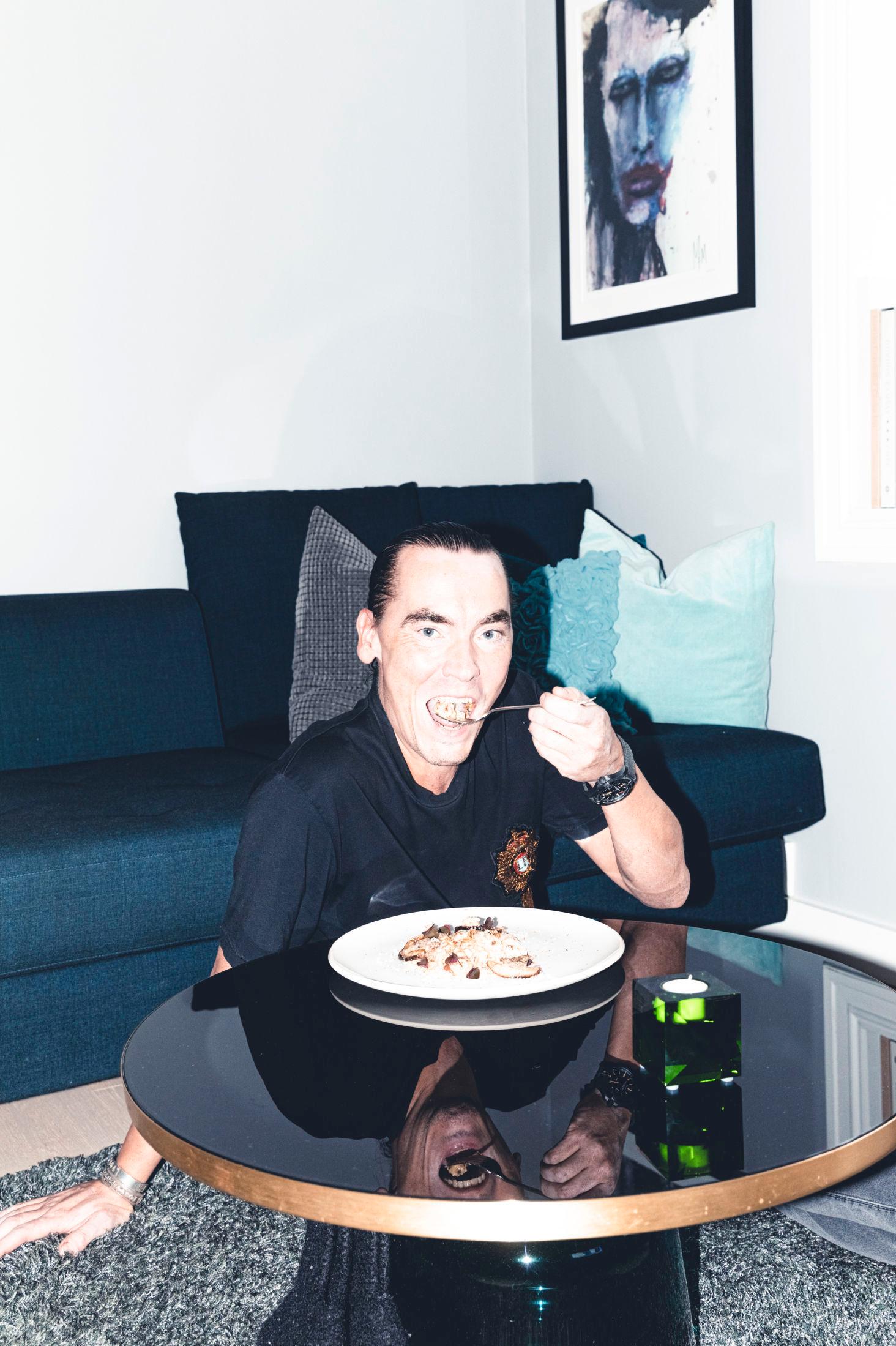 LETT HENSLENGT: 45-åringen liker aller best å spise på gulvet foran TV-en, som alltid står på danske nyheter, ifølge ham selv. Legg også merke til maleriet av Marilyn Manson på veggen over han. Foto: Krister Sørbø/VG