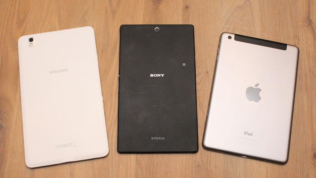 Baksiden på Xperia Z3 Tablet Compact er dørgende kjedelig, uten at det egentlig gjør noe. Til venstre Samsung Galaxy Tab Pro, som har en bakside i imitert skinn. Til høyre iPad Mini 3, som har en bakside i metall. Foto: Espen Irwing Swang, Tek.no
