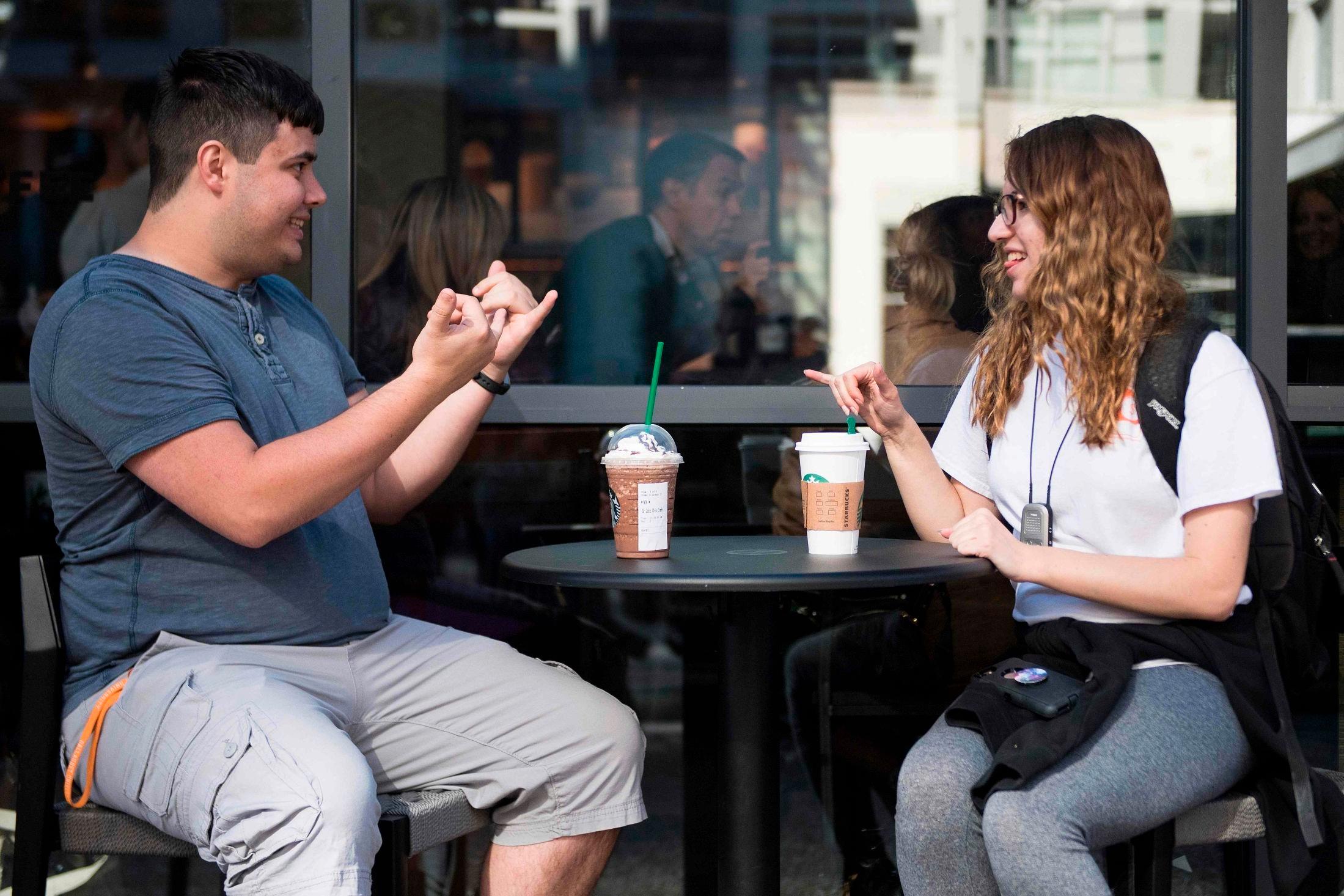 GLADE KUNDER: Tegnspråkstudentene Nikolas Carapellatti og Rebecca Witzofsky drikker kaffe ved den nye tegnspråkkafeen til Starbucks. Foto: Jim Watson/AFP