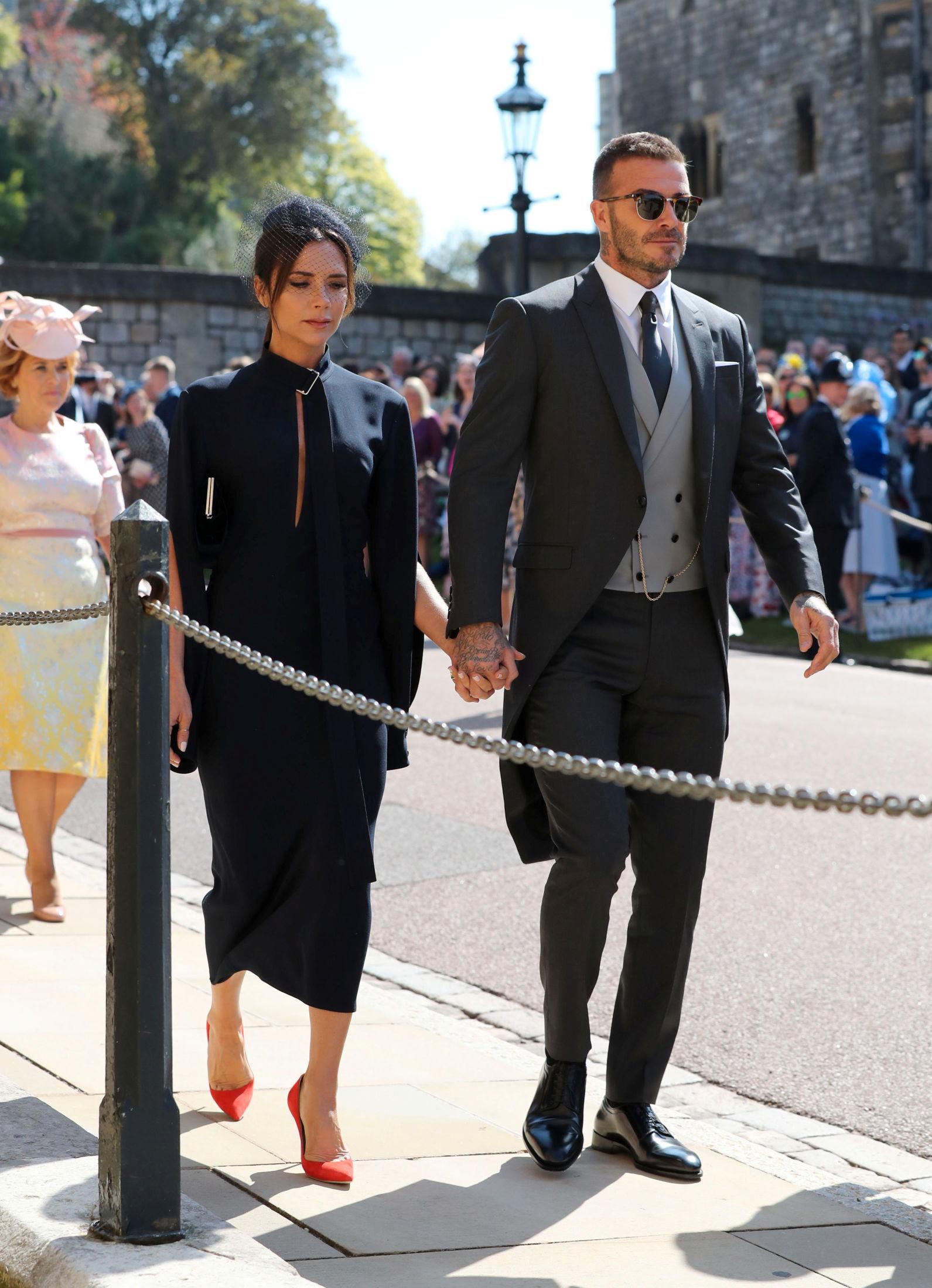 HÅND I HÅND: Ekteparet Victoria og David Beckham kom sammen i bryllupet. Victoria Beckham har selv gått ut og avkreftet at hun skulle designe brudekjolen. For anledningen hadde hun mørk kjole med røde sko. David stilte i grå sjakett. Foto: Gareth Fuller/Reuters.