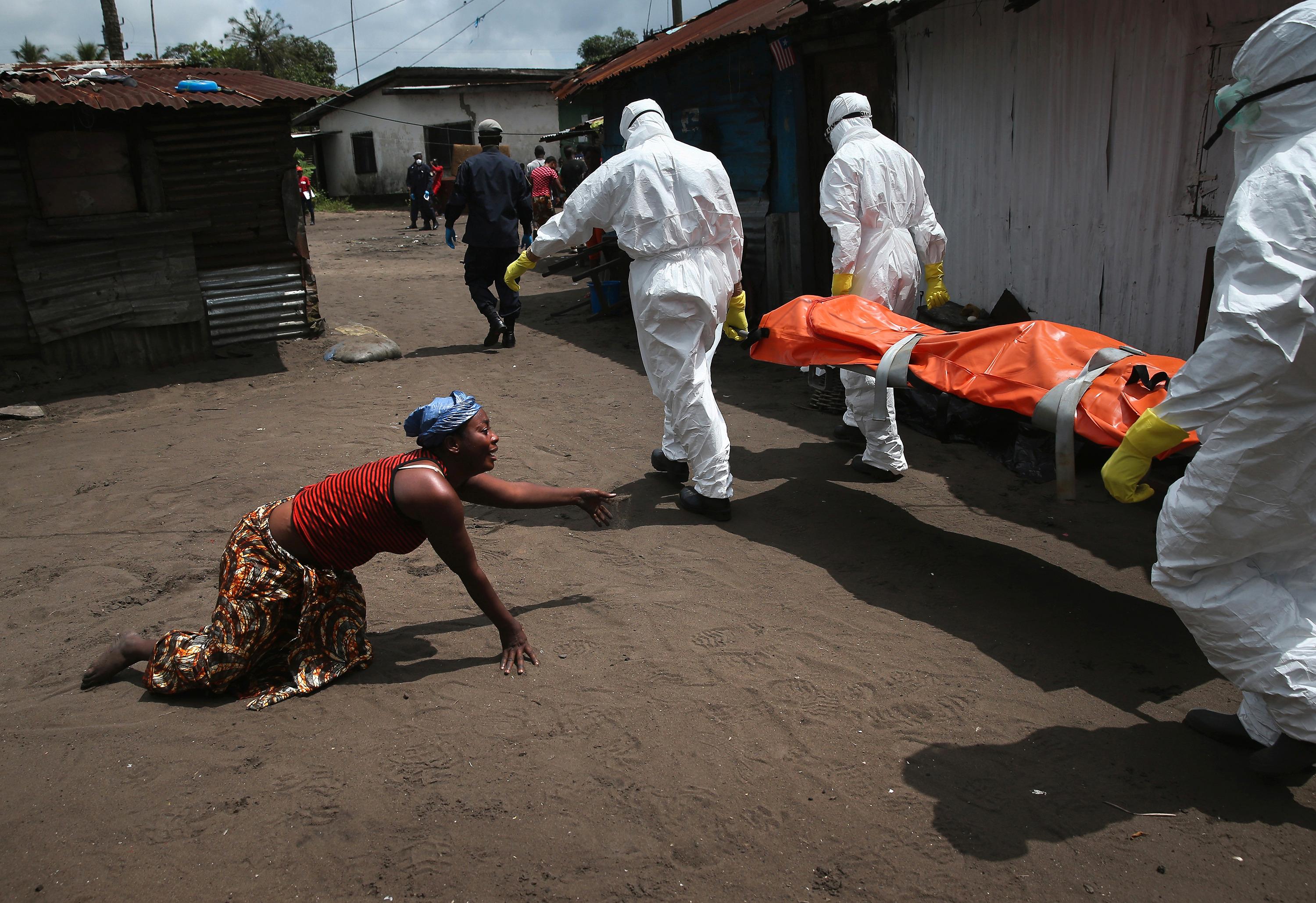 A woman crawls towards the body of her sister as Ebola burial team members take her for cremation on October 10, 2014 in Monrovia, Liberia. The woman had died outside her home earlier in the morning while trying to walk to a treatment center, according to her relatives. The burial of loved ones is important in Liberian culture, making the removal of infected bodies for cremation all the more traumatic for surviving family members. Foto: John Moore / Getty Images, United States, Shortlist, Current Affairs, Professional Competition, 2015 Sony World Photography Awards