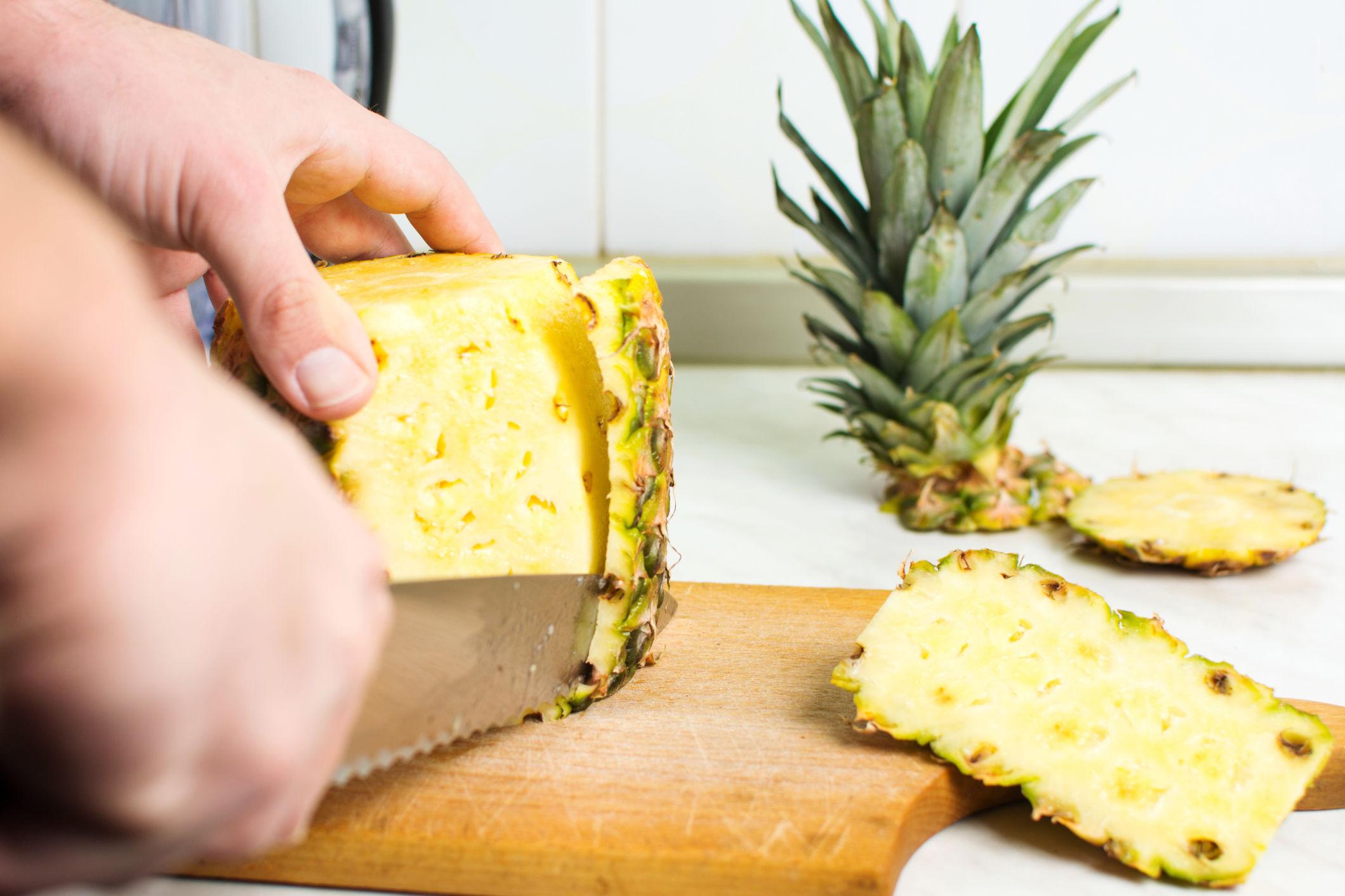 SKJÆR AV SKALLET: Ananasen står mer stødig på skjærebrettet når du kutter vekk toppen og bunnen først. Foto: Shutterstock / NTB Scanpix
