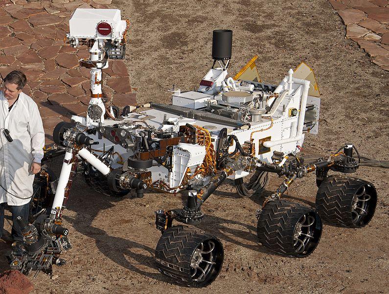 Hvis du trodde Curiosity var en søt liten Wall-E-robot, må du tro om igjen. Her står en forsker ved siden av roveren på et testområde i California.Foto: NASA