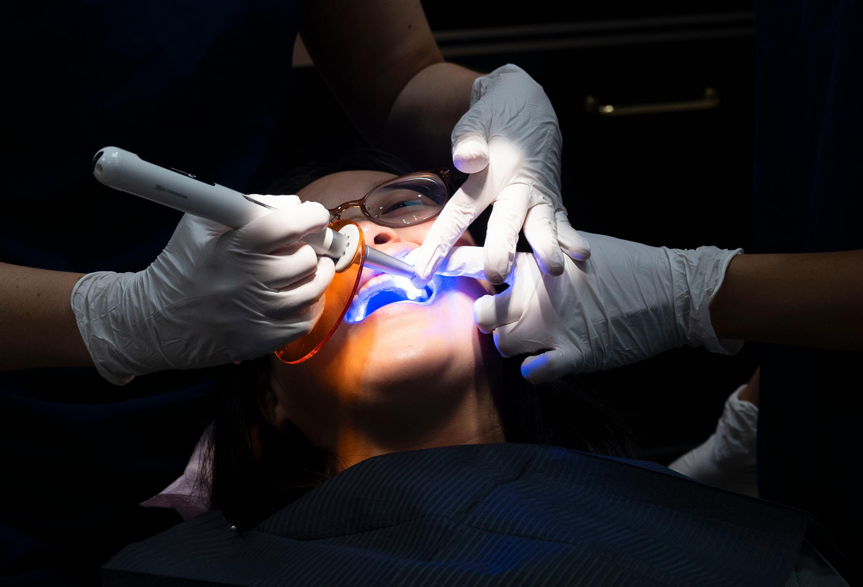 Her får Xueqi UV-lys som herder limet under tannsmykket hos tannlege Anne Myrlund Vollstad.