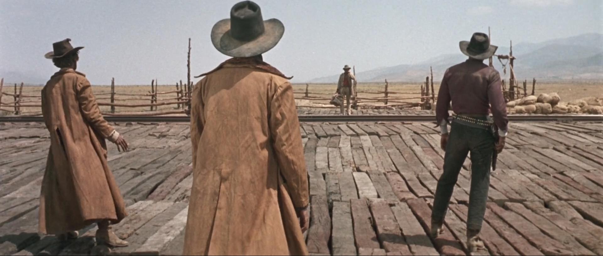 Charles Bronson spiller den navnløse, munnspill-spillende revolvermannen lengst vekk i bildet, og rød skjorte og lysere klær enn de andre i scenen. Fra filmen «Once upon a time in the West».